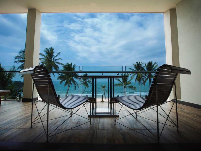 Dwa krzesła i stół na tarasie z widokiem na ocean i palmy.