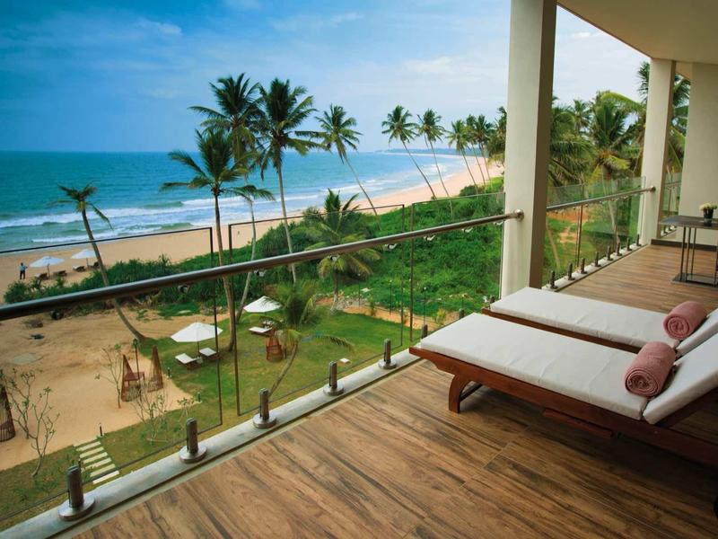 Balkon z leżakami z widokiem na plażę z palmami i niebieskim morzem.