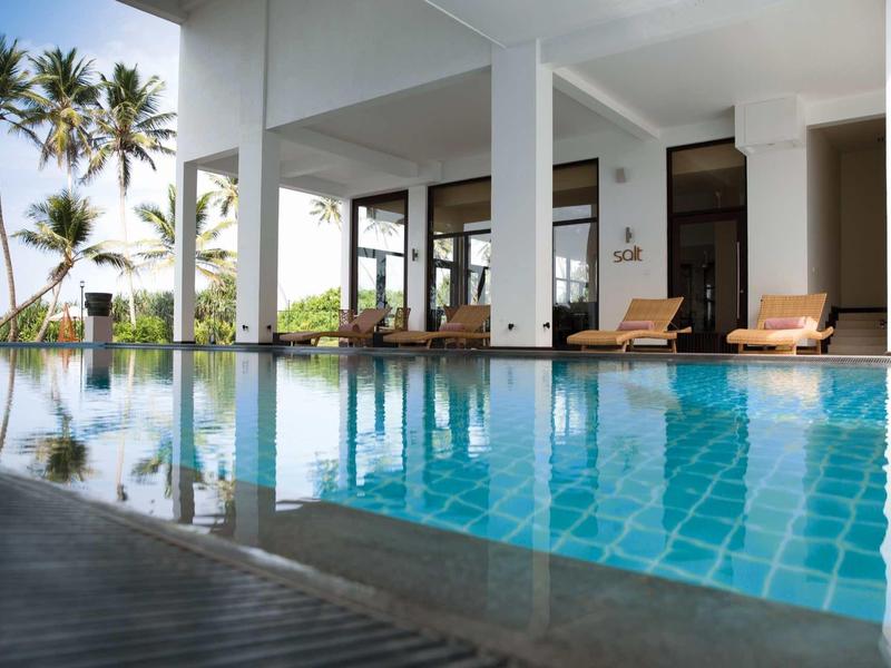 Nowoczesny obszar basenowy z leżakami i palmami, otoczony białą architekturą.