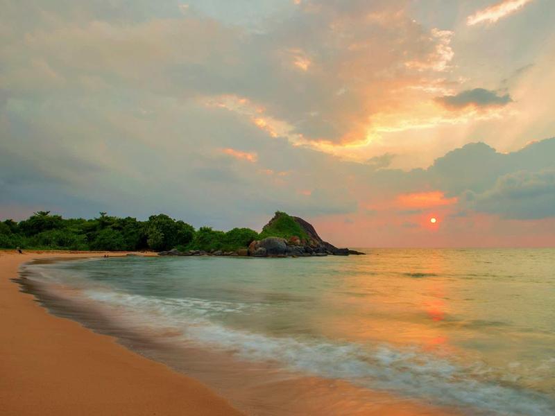 Piaszczysta plaża z spokojnym morzem i pochmurnym niebem o zachodzie słońca.