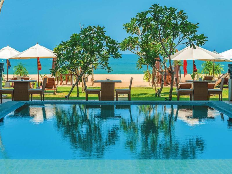 Widok na basen z leżakami i parasolami na plaży pod czystym niebem.