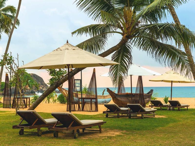 Leżaki z parasolami pod palmami na plaży z widokiem na morze.