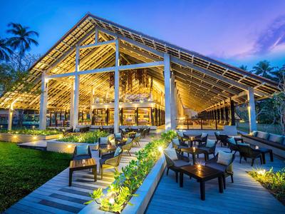 Modernes, beleuchtetes Restaurant mit offenem Dach und Holzdekor in tropischer Umgebung bei Dämmerung