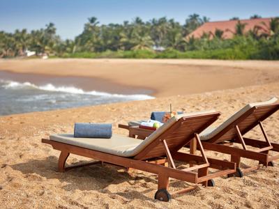 Zwei Liegestühle mit Handtüchern am Sandstrand mit Meer und Palmen im Hintergrund