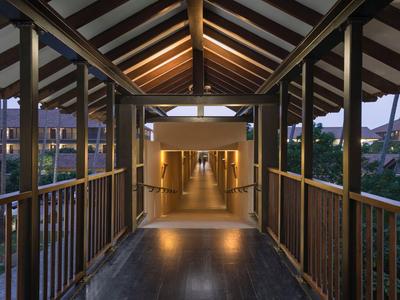 Überdachter Holzsteg mit Geländer, der zu einem beleuchteten Hotelflur führt.