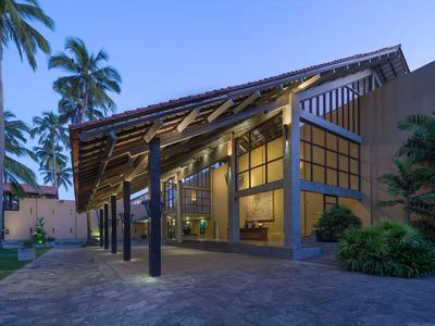 Modernes Hotelgebäude mit großer überdachter Eingangsfront und Palmen bei Dämmerung