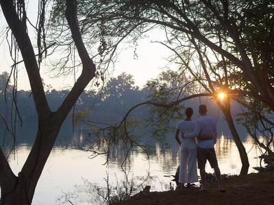 Ein Paar umarmt sich am Ufer eines Sees bei Sonnenuntergang in einer ruhigen Naturumgebung.