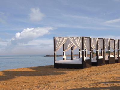 Mehrere weiße Strandbetten mit Vorhängen stehen auf sandigem Strand vor dem ruhigen Meer.