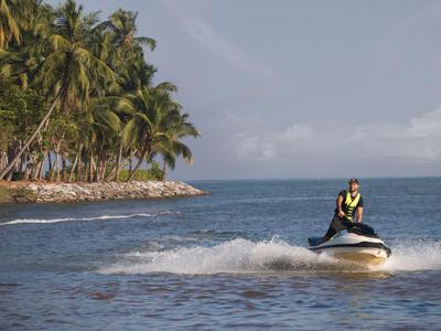 Person fährt Jetski auf dem Meer nahe einer Insel mit Palmen.