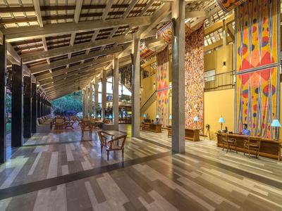 Großer, moderner Hotel-Außenbereich mit Holzstühlen, Säulen und dekorativen Wänden bei Dämmerung.