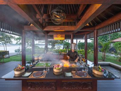 Offene Grillstation in einem hölzernen Pavillon mit einem Koch und Blick auf Garten und See