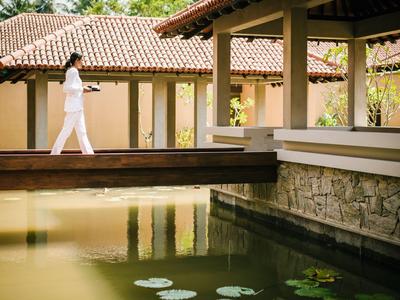 Frau in weißer Kleidung geht auf einem Steg neben einem Teich in einer Hotelanlage.