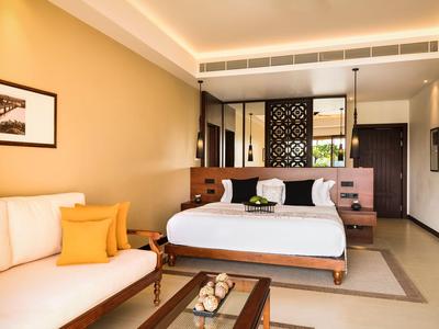 Helles Hotelzimmer mit Doppelbett, Sofa und modernem Dekor in warmen Farben.