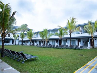 Hotel mit zweistöckigem Gebäude und Liegestühlen am grasbewachsenen Innenhof unter Palmen.