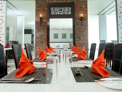 Modernes Restaurant mit weißem Tisch, schwarzen Stühlen und orangefarbenen Servietten.