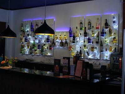 Bar mit schwarzen Hängelampen, beleuchteten Regalen voller Flaschen und einer Theke aus dunklem Holz.