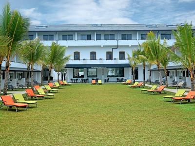 Modernes Hotel mit zwei Etagen, grüner Rasenfläche und braunen Liegestühlen unter Palmen.