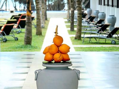 Graue Vase mit orangenen Früchten vor Palmen und Liegestühlen in modernem Außenbereich.