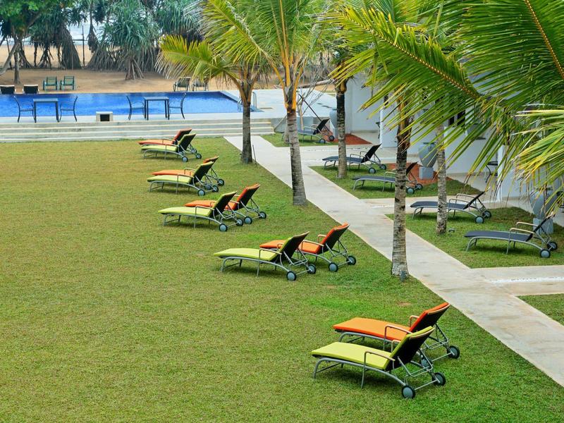 Grüne Rasenfläche mit Sonnenschirmen und Liegestühlen neben einem Pool und Palmen.