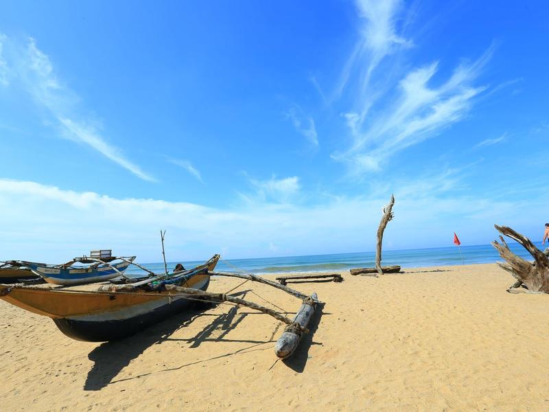 Boote am sandigen Strand unter blauem Himmel mit weißen Wolken, im Hintergrund das Meer.
