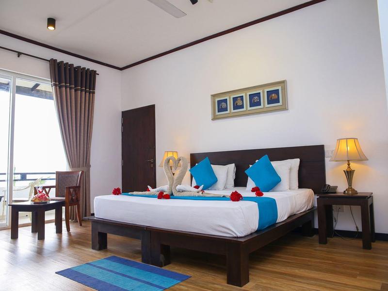 Gemütliches Schlafzimmer mit großem Bett, blauen Kissen, Holzfußboden und Balkon mit Sitzbereich.