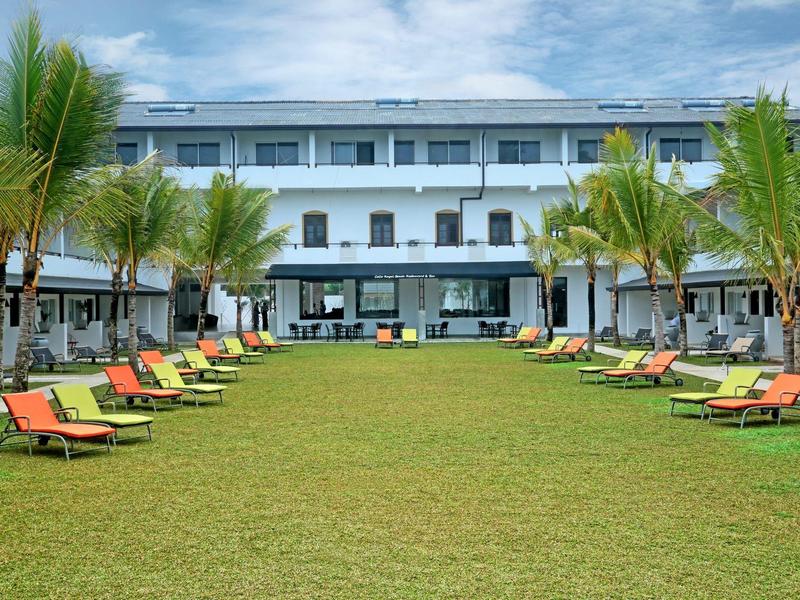 Modernes Hotel mit zwei Etagen, grüner Rasenfläche und braunen Liegestühlen unter Palmen.