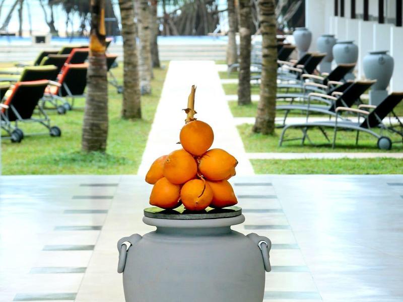 Graue Vase mit orangenen Früchten vor Palmen und Liegestühlen in modernem Außenbereich.