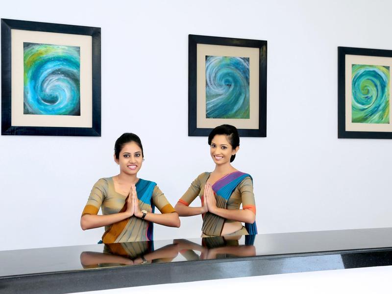 Zwei Frauen in Saris sitzen an einem Empfangstresen mit drei abstrakten Bildern an der Wand.