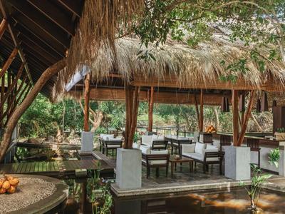 Otevřená jídelna s dřevěným nábytkem a doškovou střechou v tropickém hotelu.