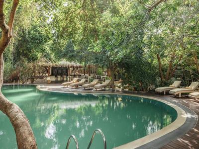 Kruhový bazén obklopený stromy a lehátky v klidném hotelovém prostředí.