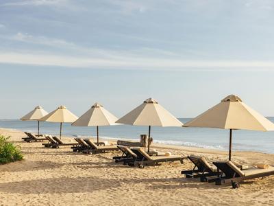 Písčitá pláž s několika lehátky a slunečníky zarovnanými u moře.