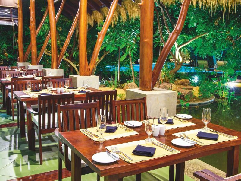 Un elegante ristorante all'aperto con mobili in legno con vista su un giardino con acqua.