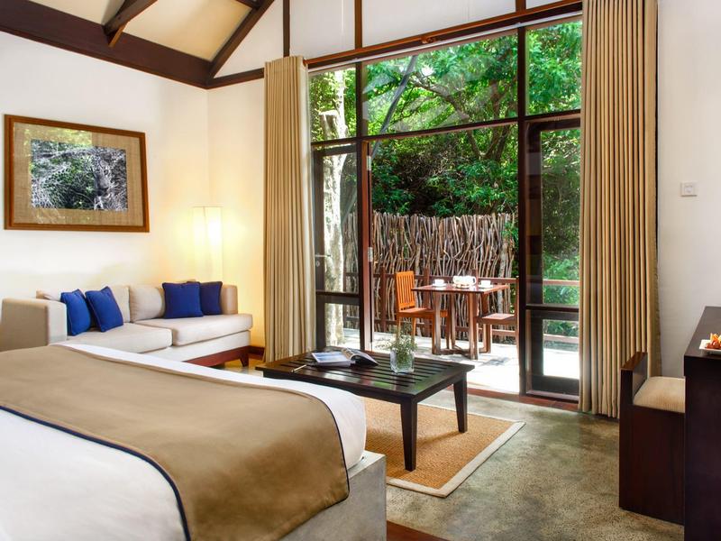 Camera d'hotel moderna con letto grande, divano e terrazza con vista su alberi verdi.