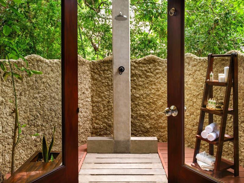 Porte aperte conducono a un piccolo spazio esterno con doccia esterna e scaffale in legno decorativo.