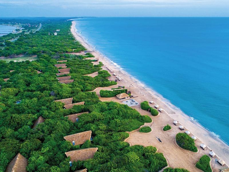 Veduta aerea di una lunga spiaggia con mare azzurro trasparente e costa verde vegetata.