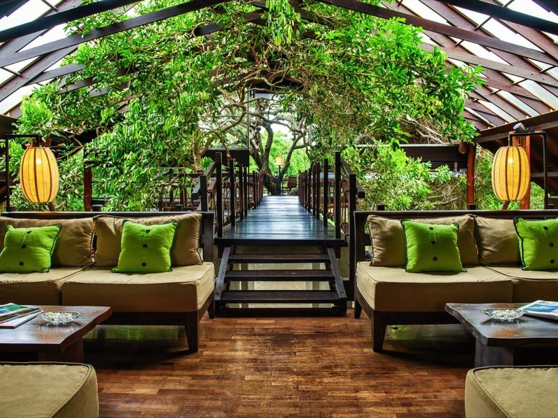 Interno di una lounge moderna con pavimento in legno, cuscini verdi e abbondante decorazione verde.