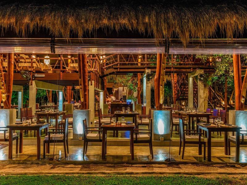 Ristorante all'aperto illuminato con tavoli e sedie sotto un tetto di paglia di notte.