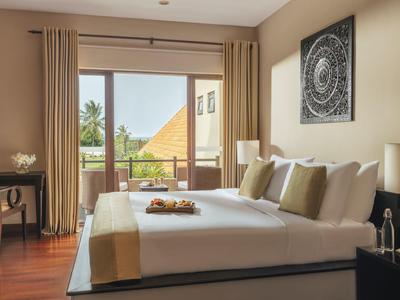 Chambre d'hôtel lumineuse avec lit double, balcon et vue sur la végétation tropicale.