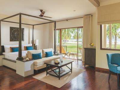 Chambre d'hôtel lumineuse avec lit à baldaquin, sol en bois et vue sur un balcon verdoyant.
