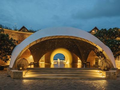 Salon moderne en forme de dôme éclairé avec des fenêtres en arc dans une cour d'hôtel au crépuscule.