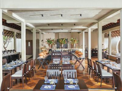 Intérieur d'un restaurant élégant avec sols en bois et colonnes blanches, tables dressées avec vaisselle bleue.