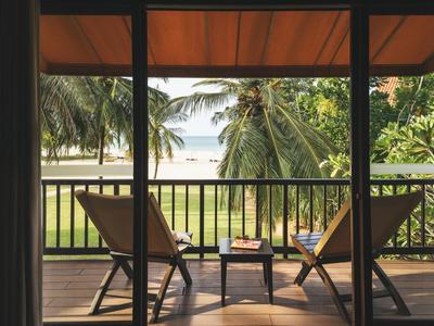 Balcon avec vue sur les palmiers et la plage, deux chaises longues et une petite table.