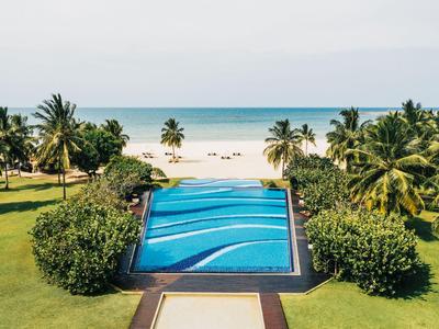 Piscina a sfioro con vista su una spiaggia tropicale e il mare, circondata da palme.