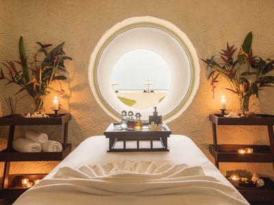 Gemütlicher Spa-Raum mit Massagebett, Kerzenlicht und Meerblick durch ein rundes Fenster