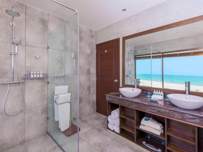 Salle de bain moderne avec doubles vasques, grande étagère en bois et vue sur la mer par la fenêtre.
