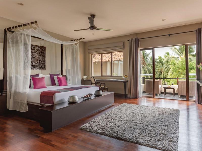 Chambre élégante avec lit à baldaquin, tapis, fenêtre donnant sur terrasse et palmiers.