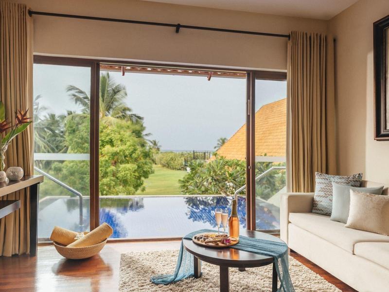 Salon moderne avec grande fenêtre donnant sur piscine, jardin et palmiers.