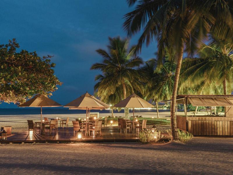 Restaurant de plage avec palmiers la nuit et espaces assis éclairés sous un ciel bleu foncé