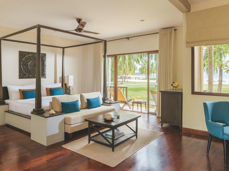 Chambre d'hôtel lumineuse avec lit à baldaquin, sol en bois et vue sur un balcon verdoyant.