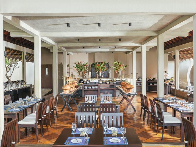 Intérieur d'un restaurant élégant avec sols en bois et colonnes blanches, tables dressées avec vaisselle bleue.